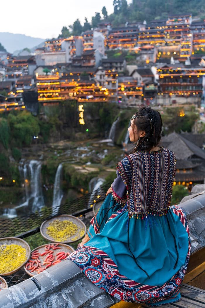 Mujer vestida con ropa tipica de la ciudad de Lijiang mirando al horizonte.