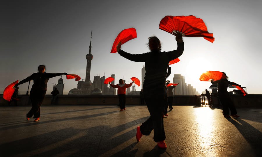 personas chinas bailando adelante de su ciudad.